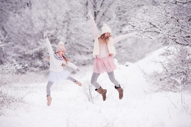 屋外で雪の中でジャンプするスタイリッシュなニットの服を着ている2人の子供の女の子