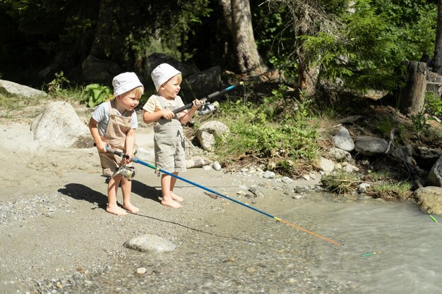 two kids boys brothers twins fishing with a fishing rod on the mountain river on summer day