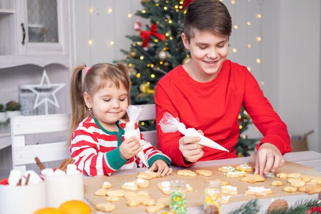 two kids brother and sister in pajamas cooking festive gingerbread in christmas decorated kitchen
