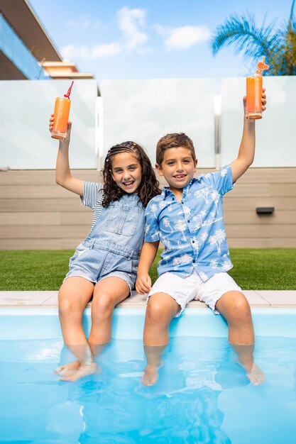 Photo two kids drinking orange juice in the swimming pool