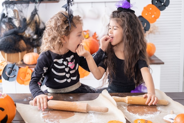 Two kids girl in costume of witch, baking cookies, having fun in kitchen, celebrating Halloween.