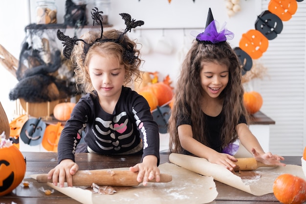 Two kids girl in costume of witch baking cookies having fun in kitchen celebrating halloween