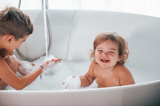 Due bambini che si divertono e si lavano nella vasca da bagno a casa in posa per una macchina fotografica