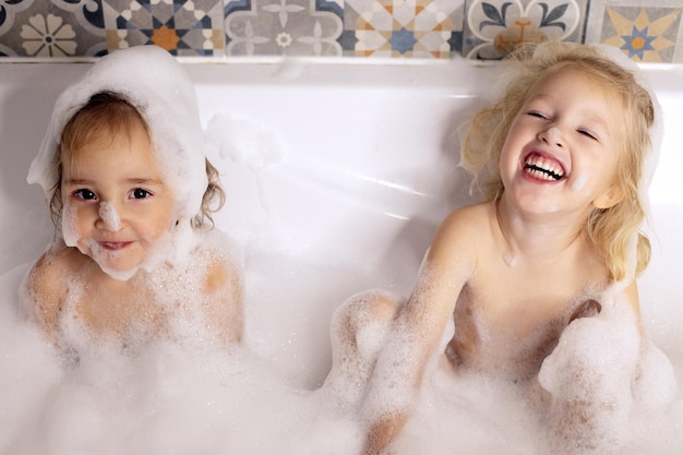 Photo two kids little girls sisters having fun in bathroom playing with bath foam. kids personal care. beautiful cheerful kids. carefree childhood. personal and health care