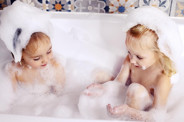 Two kids little girls sisters having fun in bathroom playing with bath foam kids personal care