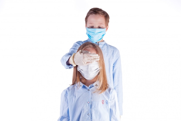 Two kids in medical protective masks against white background. Boy closes girl's eyes with his hand in a latex glove.