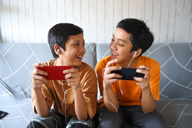Фото Двое детей разговаривают, играя в игры на смартфоне дома. современная связь и зависимость от гаджетов.