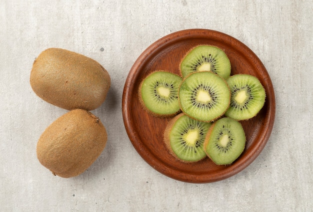 Two kiwis with slices on a wooden board.