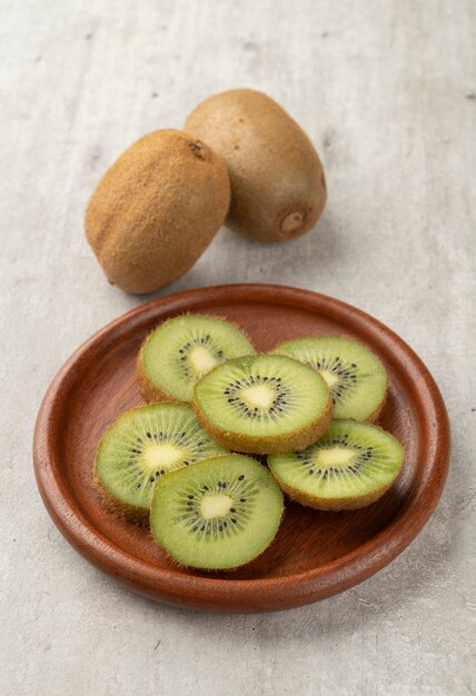 Two kiwis with slices on a wooden board.