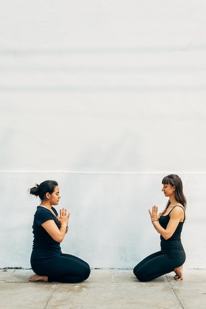 Two kneeling women dressed in black face to face in yoga position on the street Copy space