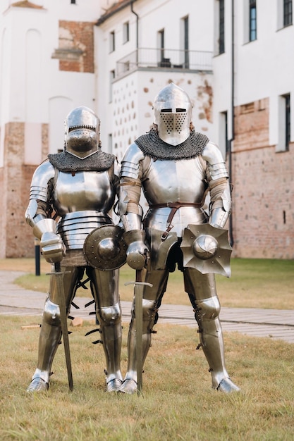 Two knights in ancient metal armor stand at the stone wall of the castle