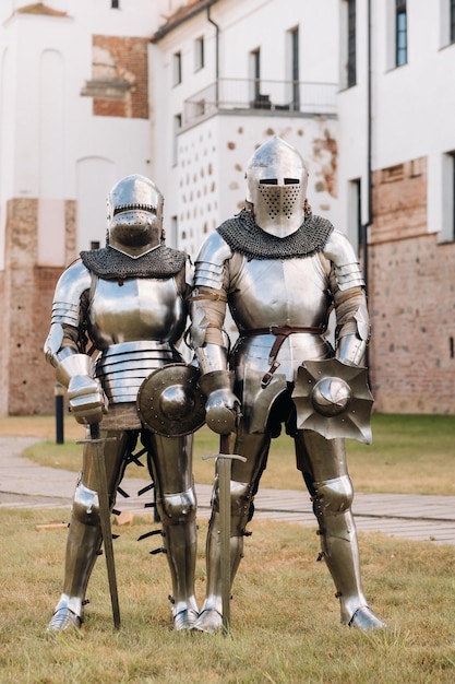 Two knights in ancient metal armor stand at the stone wall of the castle