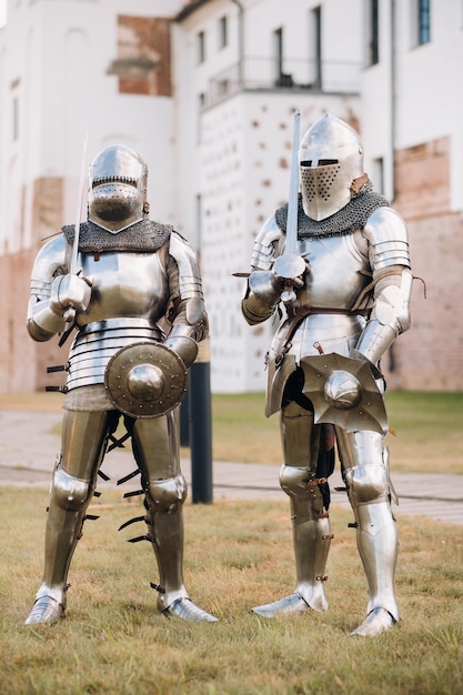 Two knights in ancient metal armor stand at the stone wall of the castle