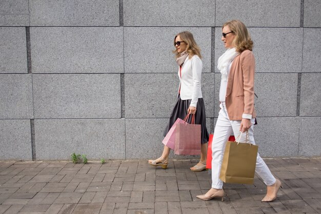 Two Ladies Carrying Paper Bags Outdoors