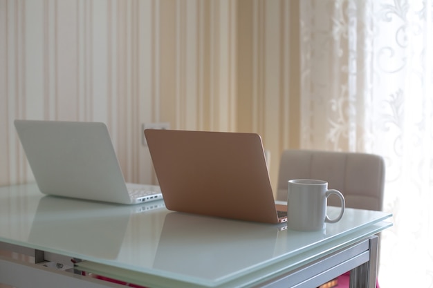 Two laptops on the kitchen's table and a cup of tea. Remote work