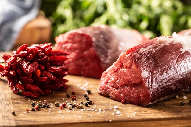 Two large pieces of sirloin meat next to a bunch of fresh chillies and peppercorns