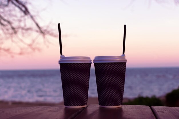 Photo two lattes are standing on a table on the beach. at the back you can see the sunset. high quality photo