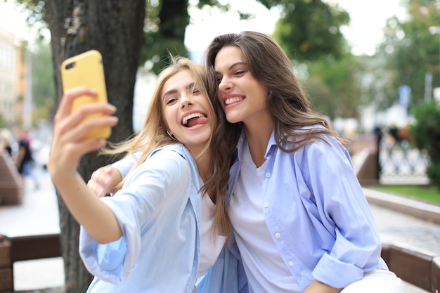 Two laughing friends enjoying weekend together and making selfie on city background.