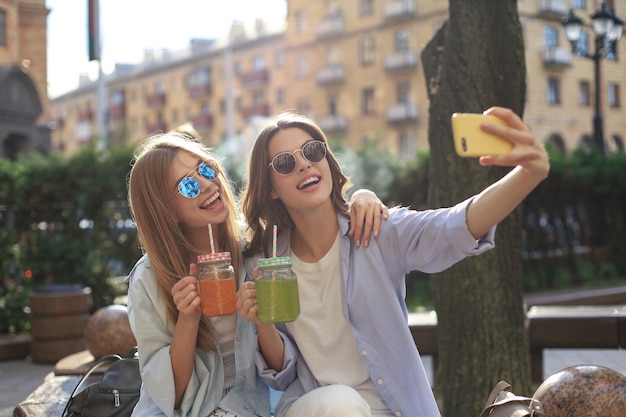 Two laughing friends enjoying weekend together and making selfie on city background.