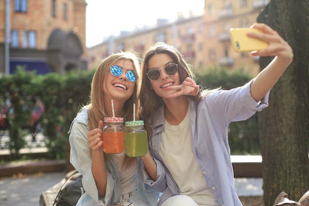 Two laughing friends enjoying weekend together and making selfie on city background.