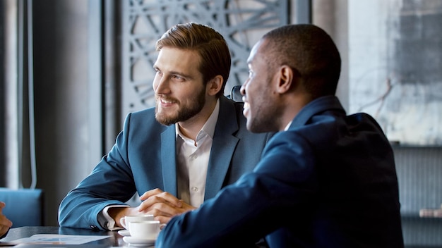 Two laughing young businessmen in suits at a meeting