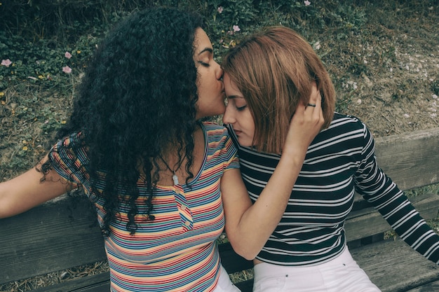 Photo two lesbian couple of different racial ethnic kissing on a bench