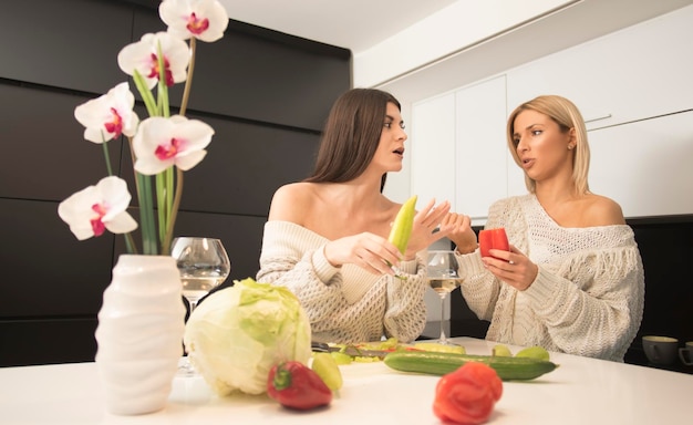 two lesbian female friends making salad in the kitchen and drinking wine from a wine glasses