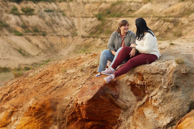 Two lesbians sitting on hill outdoors talking and laughing together