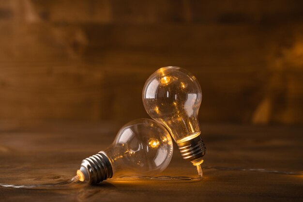 Two light bulbs leaning on each other with a wood background