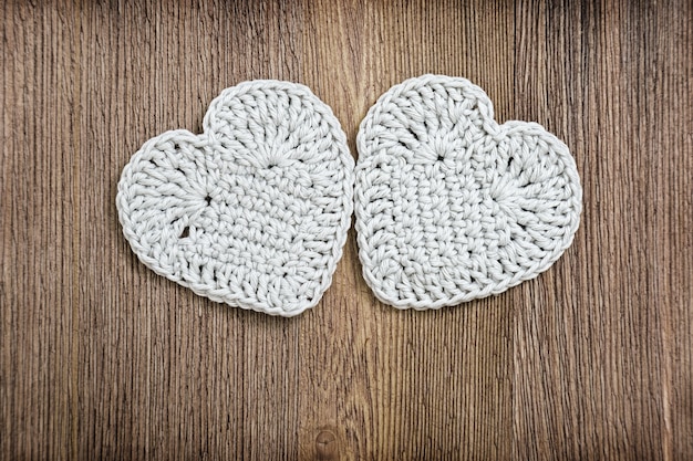 Two light gray knitted hearts on old natural wood 