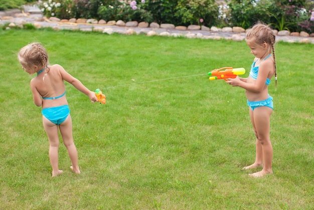 Two little adorable girls playing with water guns in the yard