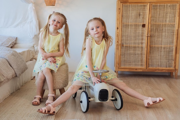 Photo two little blonde caucasian girls in yellow dresses playing at home together looking at camera