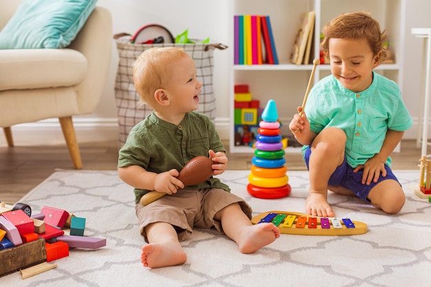 Due ragazzini stanno suonando strumenti musicali per bambini i bambini felici sono seduti sul pavimento nella stanza dei giochi e giocano