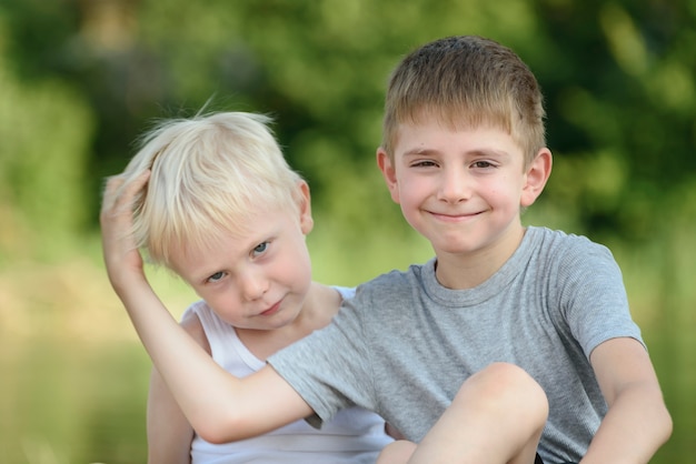 두 명의 작은 소년이 야외에 앉아 있습니다. 거리에서 흐린 된 푸른 나무입니다. 우정과 형제애의 개념