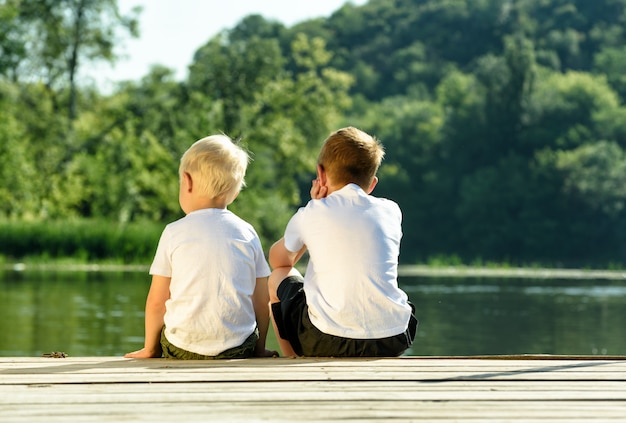 Two little boys are sitting the pier on the river bank.  of friendship and fraternity. Back view