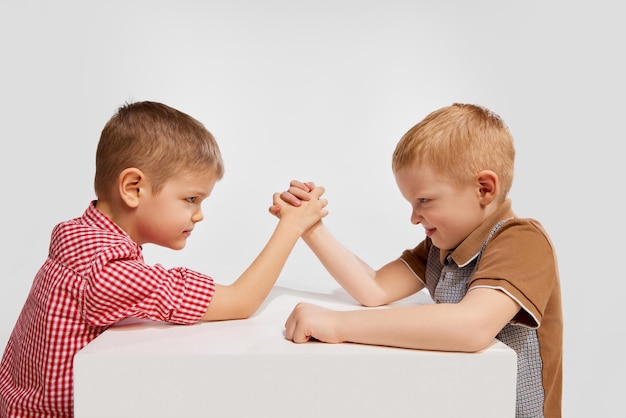 Photo two little boys children playing together in armwrestling posing against grey studio background