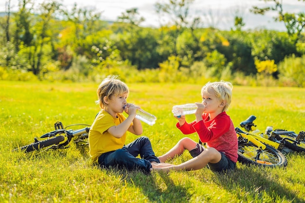 Two little boys drink water in the park after riding a bike.