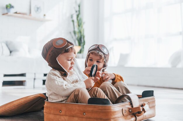 Two little boys have fun and sitting in suitcase indoors at daytime