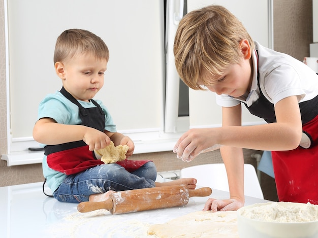 Two little boys knead the dough on the kitchen table
