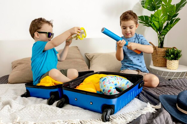 Two little boys with blue shirts ready for vacation. Happy children packing clothes into a suitcase for travel. Tourist, joy of holiday. Kids at home, preparing for flying. Modern and cozy interior.