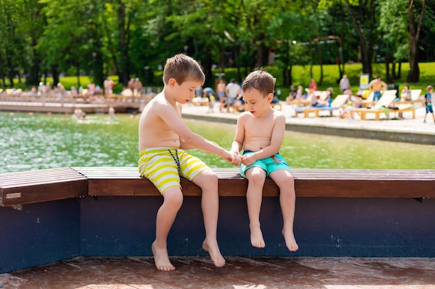 Two little brother boys are playing on the riverbank hugging rejoicing sunbathing in the sun