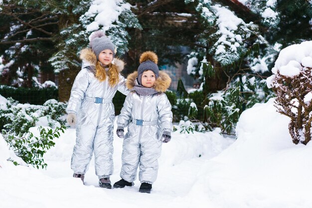 Two little cheerful children on snowy frosty day brother and sister play outdoors in winter in a ski...