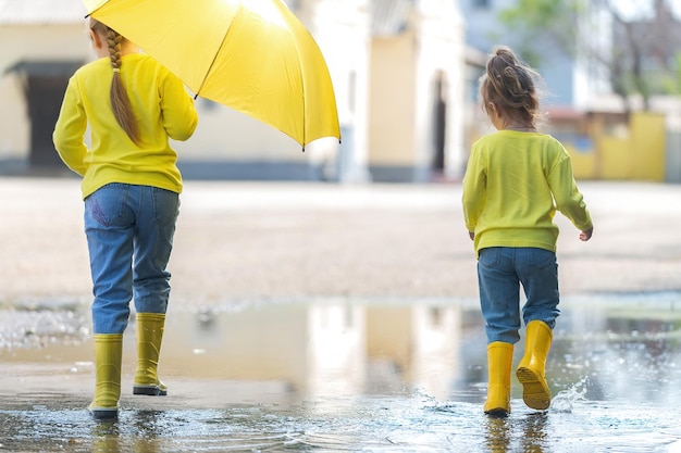 Two little cheerful girls with bright yellow and orange
umbrellas run through the puddles