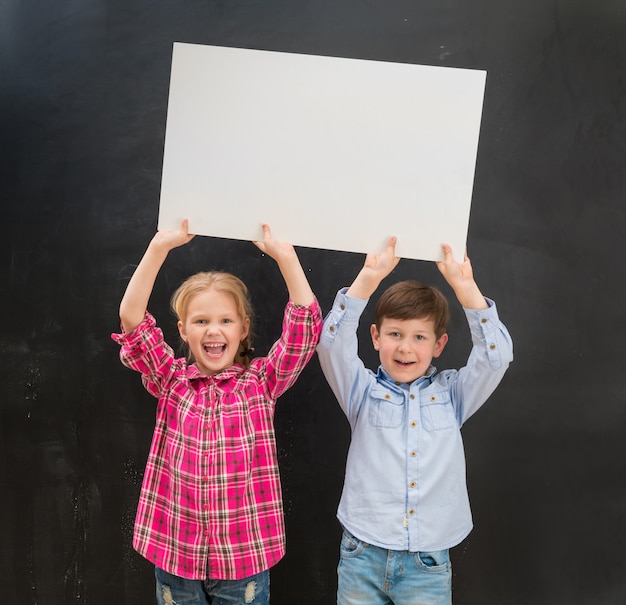 Foto due bambini piccoli che tengono il foglio di carta bianco sopra le loro teste