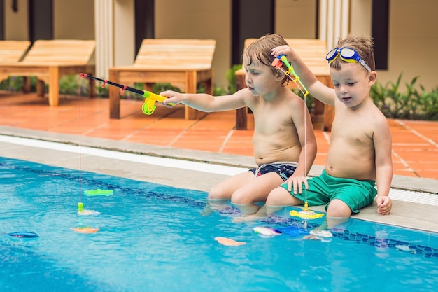 Two little cute boy is catching a toy fish in the pool.