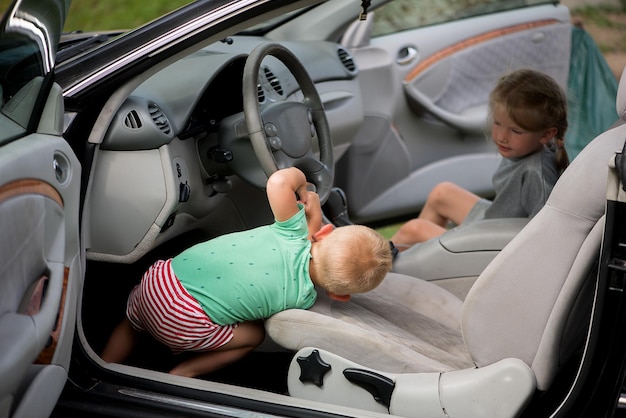 2 人の小さなかわいい子供、兄と妹が車のハンドルを握って遊んでいます。