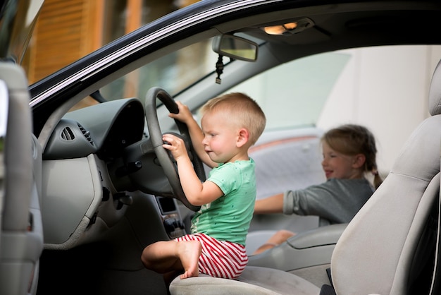 2 人の小さなかわいい子供、兄と妹が車のハンドルを握って運転して遊んでいます。