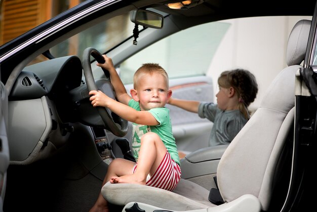 2 人の小さなかわいい子供、兄と妹が車のハンドルを握って運転して遊んでいます。