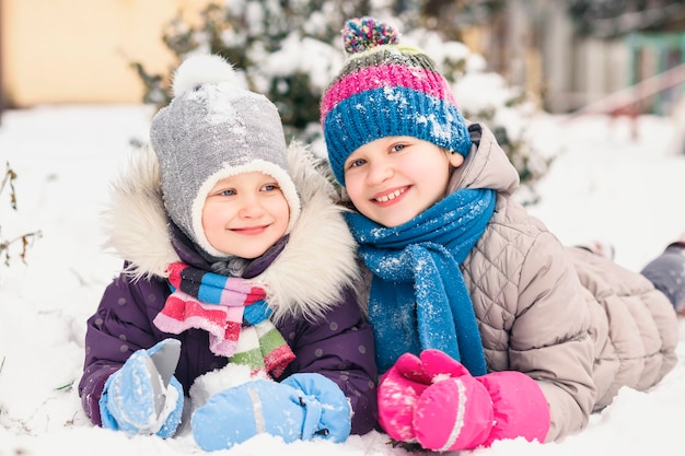 Two little girls are lying in the snow next to each other.