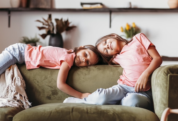 Two little girls are relaxing on the sofa in the living room. The sisters spend time together. Children's friendship